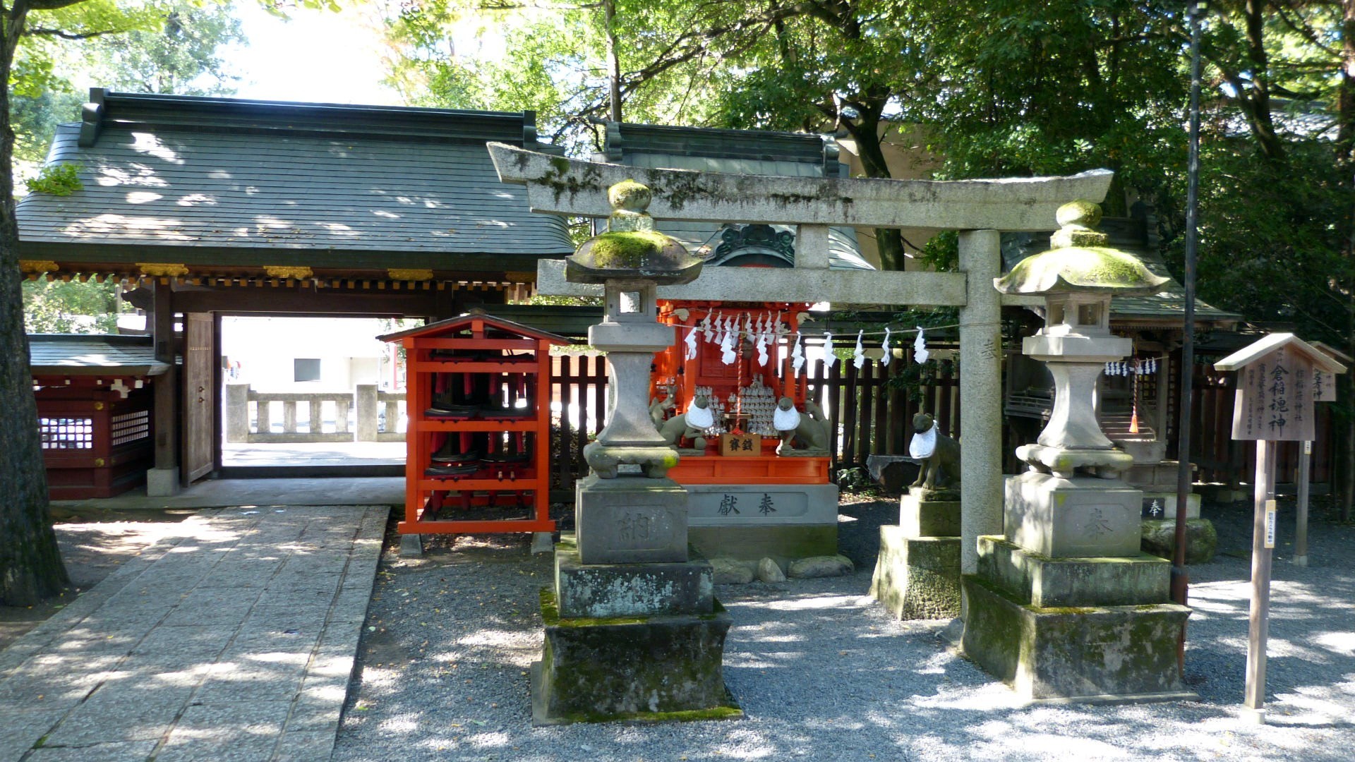 shrine grounds showing a small torii gate and two traditional stone lanterns.  The gateway is in the near distance.